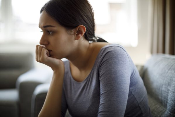 Upset woman sitting on sofa alone at home experiencing grief after adoption