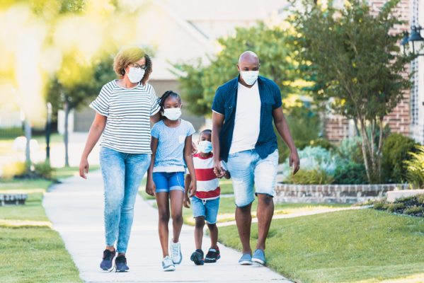 A happy family wear face masks while walking in their neighborhood during the COVID-19 pandemic.